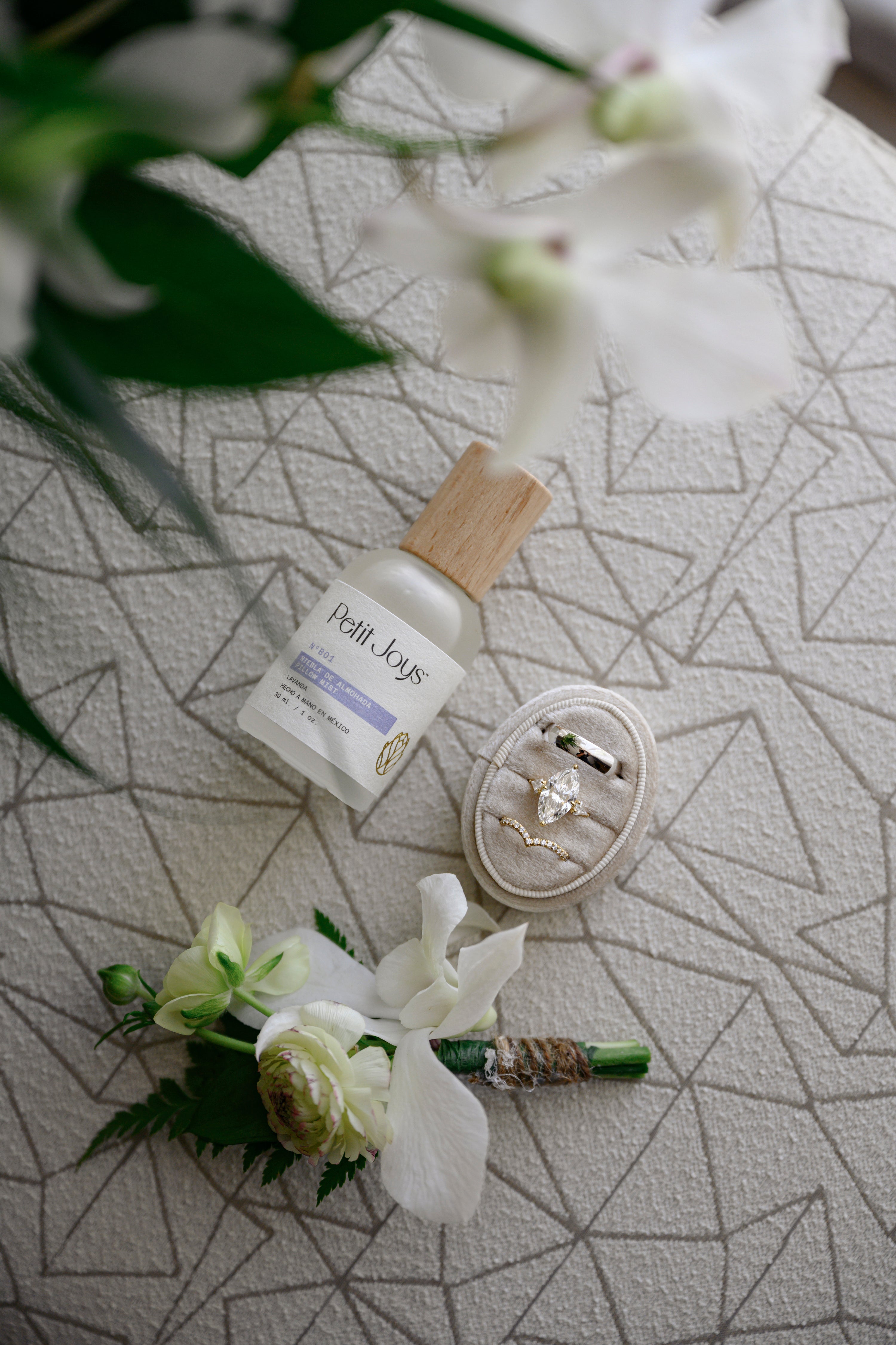 Petit Joys product, ring, and white flowers on a geometric-patterned surface