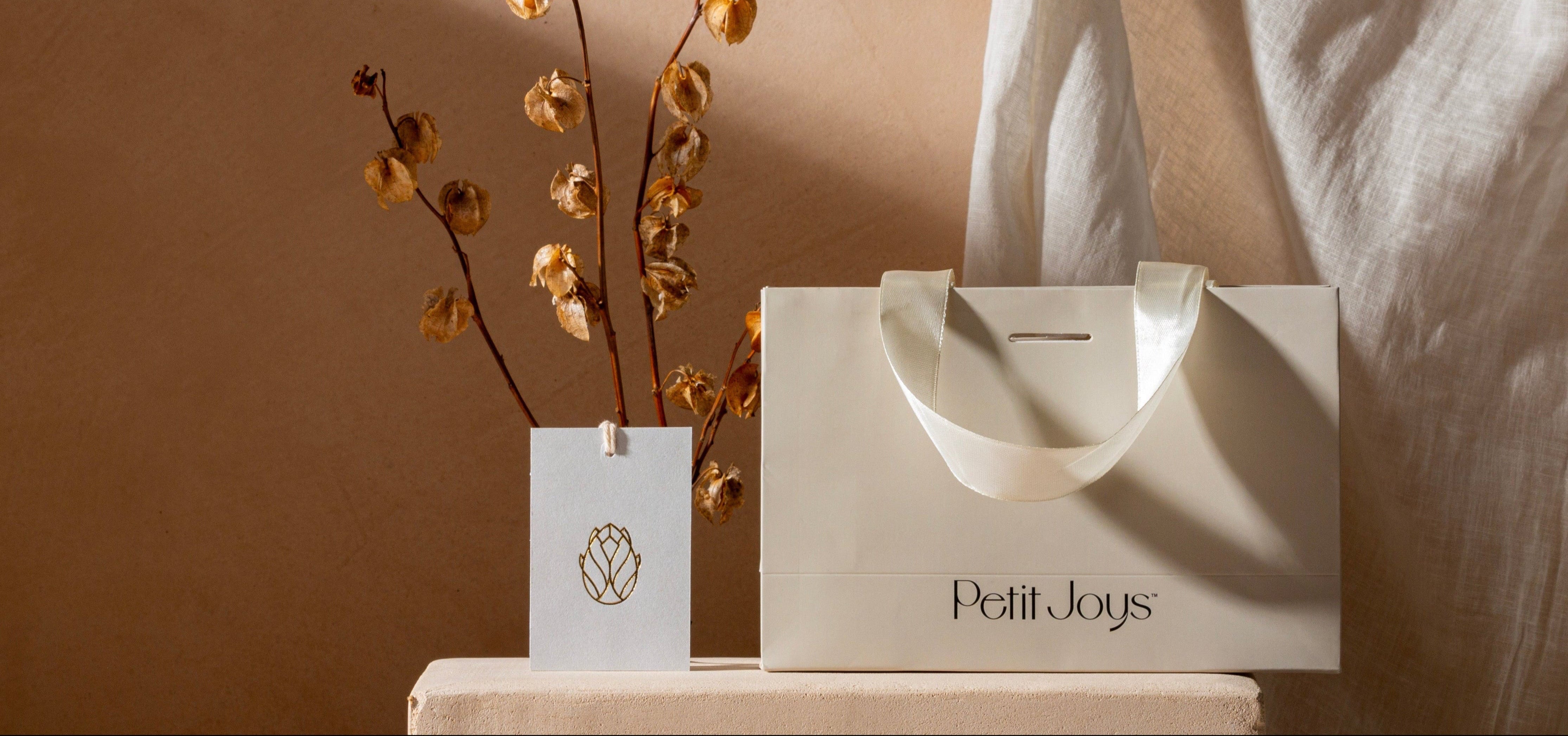 Petit Joys shopping bag and decorative vase on a wooden surface with a neutral background