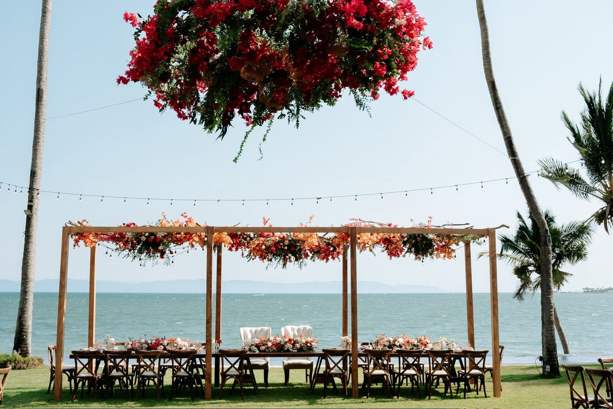 A long wedding table under a flowered pergola facing Banderas Bay